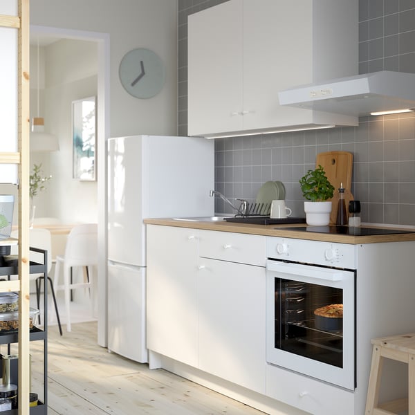 Modern kitchen with white cabinets, clock, oven, & sink. Green plant and dishes are on the counter.