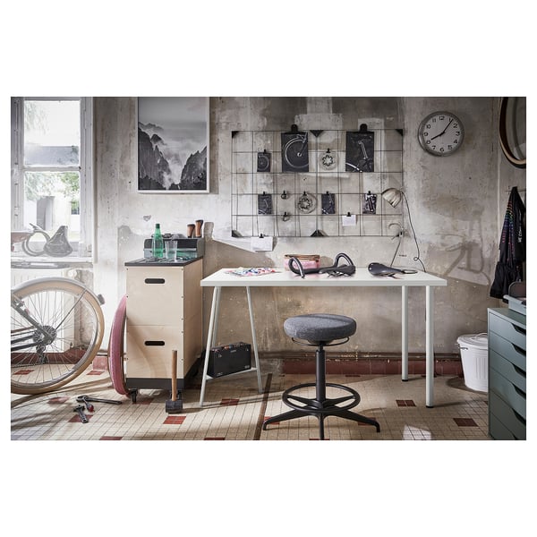 Industrial-themed workspace with white desk, grey stool, bikes, and wall art.