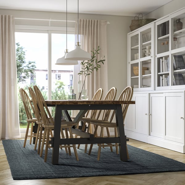 Modern dining room with blue jute rug, wooden table, chairs, pendant light, and glass cabinet.