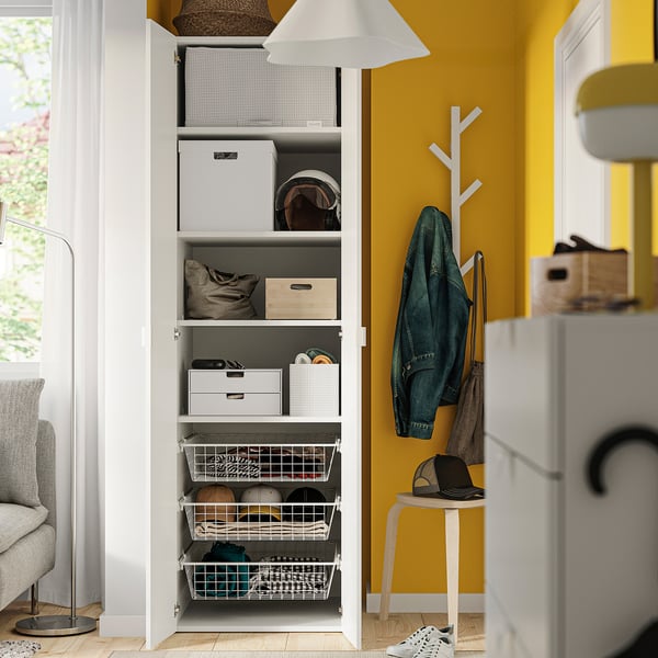 Open white wardrobe with storage boxes and baskets, yellow wall, green jacket hanging.