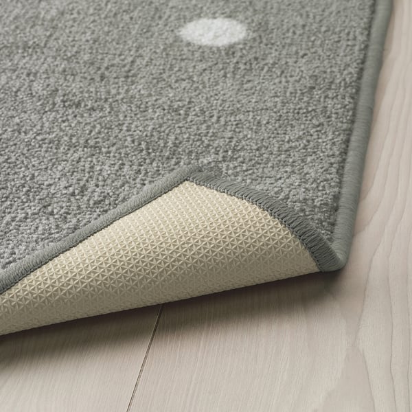 A grey rug with white dots on a wooden floor, featuring a textured rubber backing for anti-slip grip.