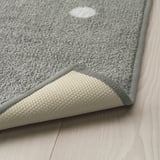 A grey rug with white dots on a wooden floor, featuring a textured rubber backing for anti-slip grip.