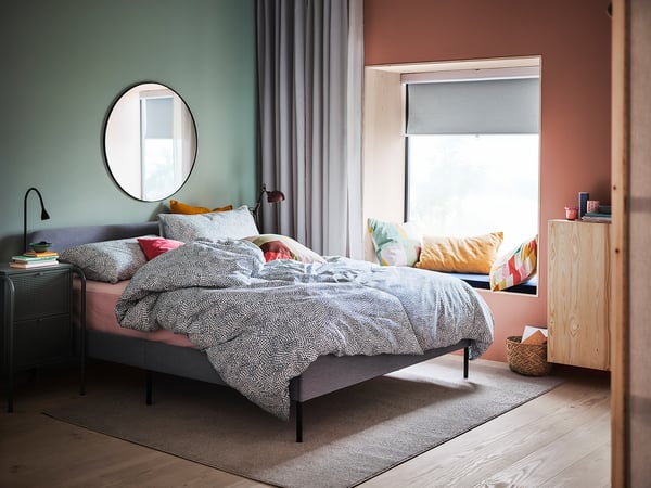 Cozy bedroom with black-framed round mirror, colorful pillows, and wooden furniture.