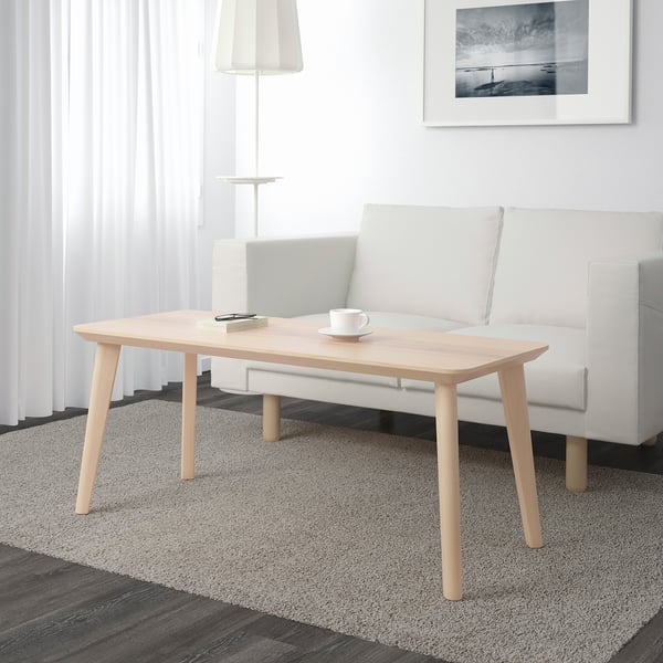 Minimalist living room with wooden coffee table, mug, notepad. Gray sofa, lamp, striped rug.