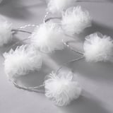 String lights with multiple white mesh pom-poms creating a festive ambiance.