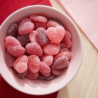 Bowl of pink heart-shaped gummy candies, likely LÖRDAGSGODIS, on a red cloth.