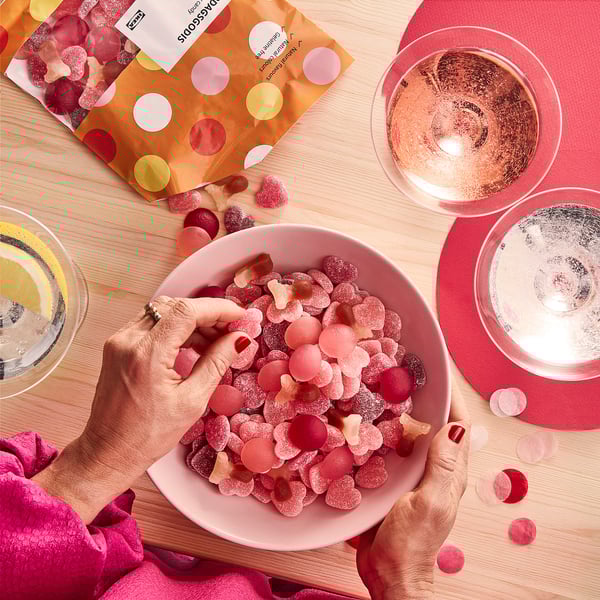 Person holding pink gummy bowl, open packaging, candies on table with placemats and glasses.