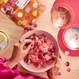 Person holding pink gummy bowl, open packaging, candies on table with placemats and glasses.