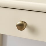 Gold-colored round doorknob on a white drawer, highly polished, showing excellent craftsmanship and quality.