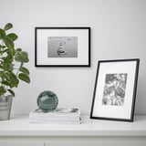 White shelf with black photo frames: one holds a boat photo, another a butterfly. Decorated with green plant and glass sphere.