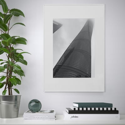Modern living room with LOMVIKEN black & white skyscraper photo frame, metal edge, surrounded by books and green plant.