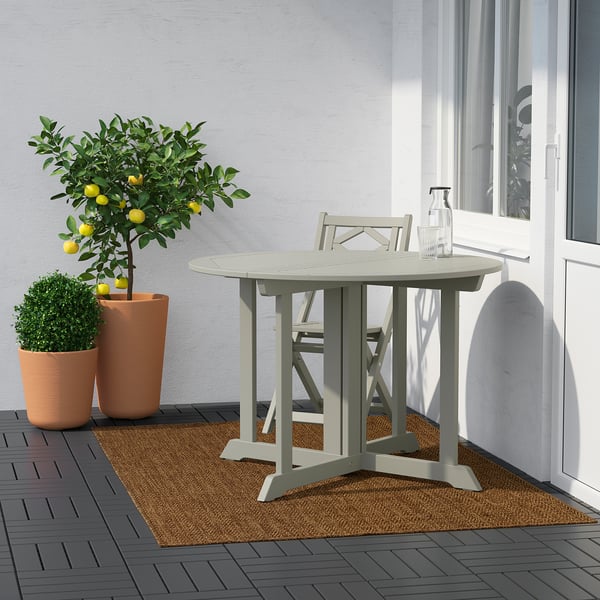 Modern patio with round LYDERSHOLM table, chairs, plants, and lemon tree beside a grey wall and white window.
