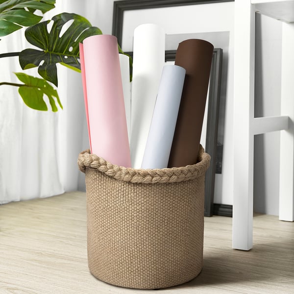 Basket holds rolled items, made of jute with woven edge, sits on floor.