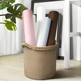 Basket holds rolled items, made of jute with woven edge, sits on floor.