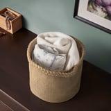 Jute basket with white blankets on wooden table. Small jewelry box on left.