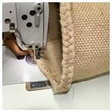 Person sewing beige jute basket with braided edge using white sewing machine.