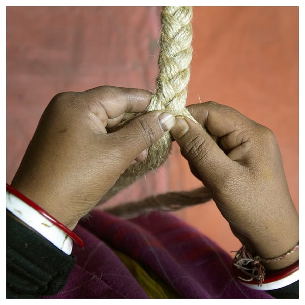 A person weaves a light-colored rope, showcasing MÄVINNs jute basket craftsmanship.