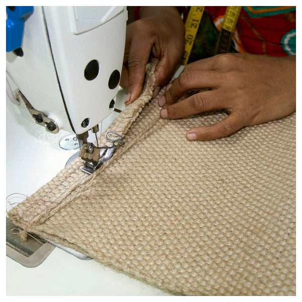 Person sewing jute material on a white sewing machine.
