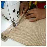 Person sewing jute material on a white sewing machine.