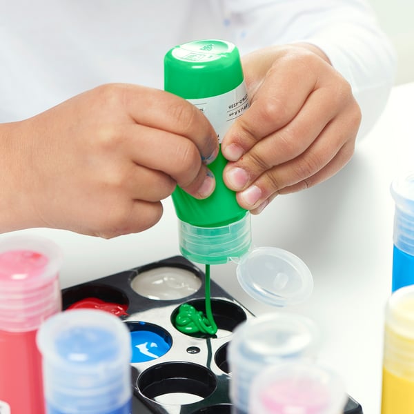 In a child is squeezing green MÅLA paint from a bottle into a tray for art activity. The paint is ready-to-use and comes in easy-to-squeeze bottles.