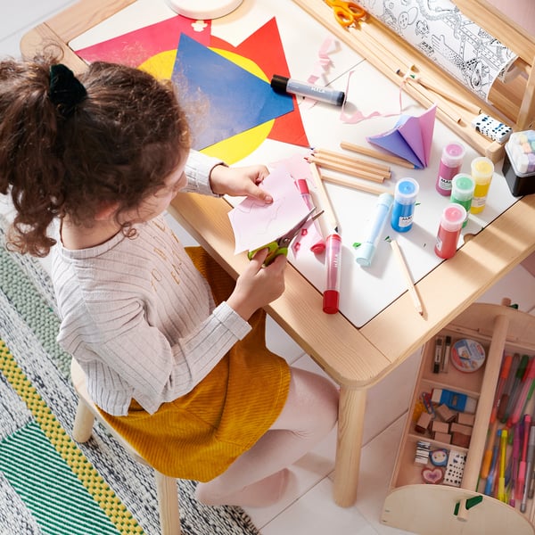 A child crafts with colorful paper and paint at a wooden table.