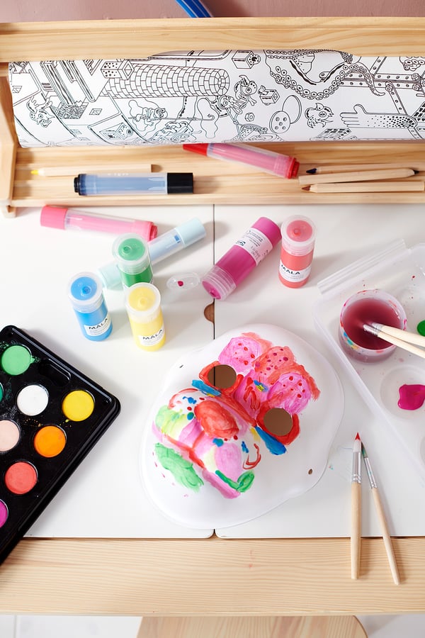 Art supplies on a table: a painted butterfly, paint bottles in various colors, brushes, and a drawing book.