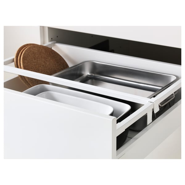 White kitchen drawer with compartments, including a large metal tray, small plastic containers, and cork trivets.