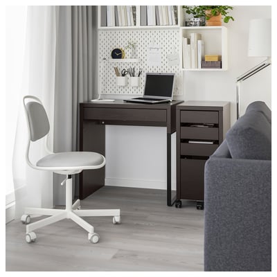 Home office setup: dark brown desk, white office chair, laptop, shelves with books, grey flooring.