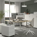 Home office setup with MITTZON adjustable white desk, gray chair, computer, and storage cabinet.