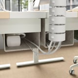 Cable management tray under desk, holding white charging cube and cables.