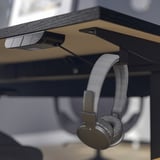 Wireless headphones hang on hook beneath modern desks sleek surface and cable management tray.