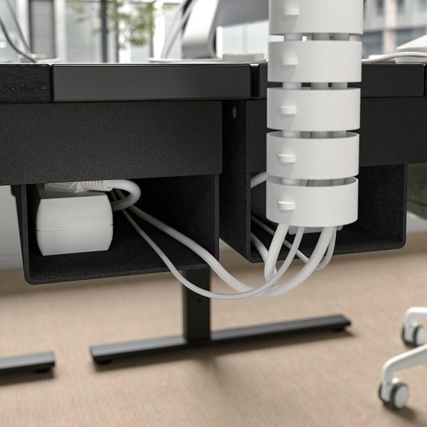 Under-desk cable management tray with white cords and connectors. Despot ensuring neat and organized cable handling.