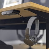 Desk with dual motors for smooth sit/stand transitions, featuring headphone hooks.
