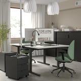 Modern home office featuring MITTZON desk, black with white top, green chair. Two hanging lamps, computer setup, minimalist decor.