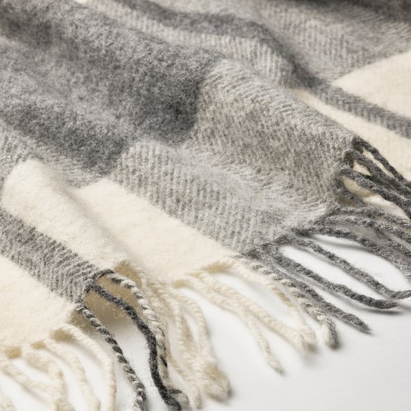 Close-up of a cozy, light grey wool throw with a soft, brushed texture and traditional check pattern. Fringes are visible along the edges.