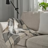 MYRULL throw blanket in light grey on couch, covers cushions, fringed ends.