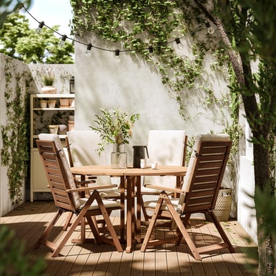 Outdoor patio set with wooden table, four matching chairs, and string lights overhead. Chairs have beige cushions.