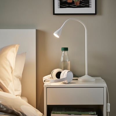 Modern NÄVLINGE lamp on nightstand with adjustable light, headphones, bottle, books.