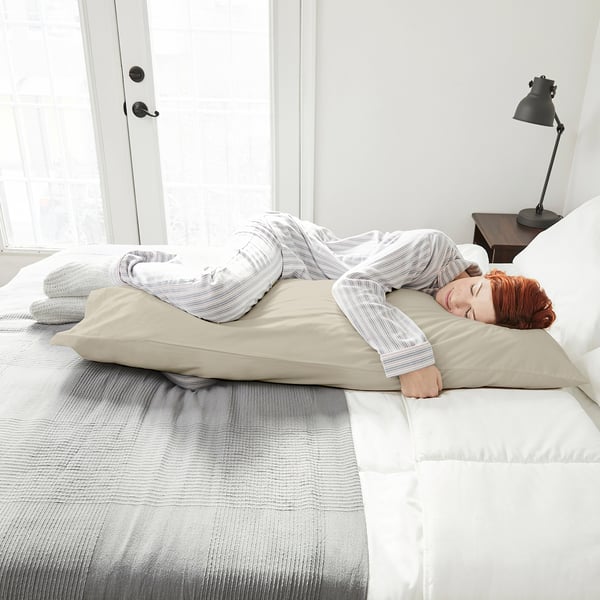 Woman sleeps on large,rectangular NONNEA pillow, light beige, crisp white bedding.