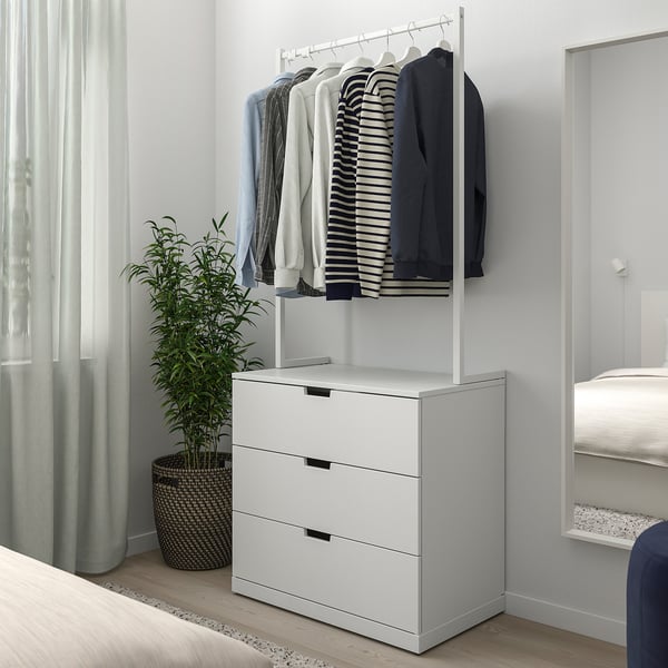 Minimalist bedroom with white NORDLI 3-drawer chest under clothes rail, green plant beside, between bed and window.