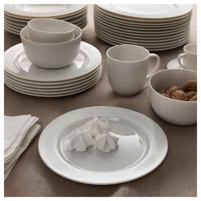 White porcelain dinnerware set, including plates, bowls, and cups, neatly stacked and arranged on a table, some plates hold meringues and walnuts.