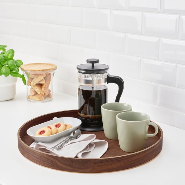 Wooden tray with black french press, two green mugs, cookies, and utensils, perfect for serving and decor.