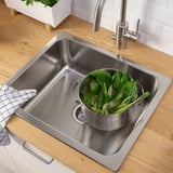 Stainless sink with colander full of green veggies on counter.