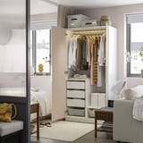 Closed wardrobe with open door, clothes inside, light on, drawers below.