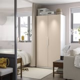 Minimalist bedroom with PAX wardrobe, beige doors, storage boxes between two windows, taller than bed and chair.