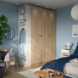 Cozy bedroom with large brown PAX wardrobe, nightstand, comfortable bed, and toys. Blue walls, mirror, chair, and pendant light.