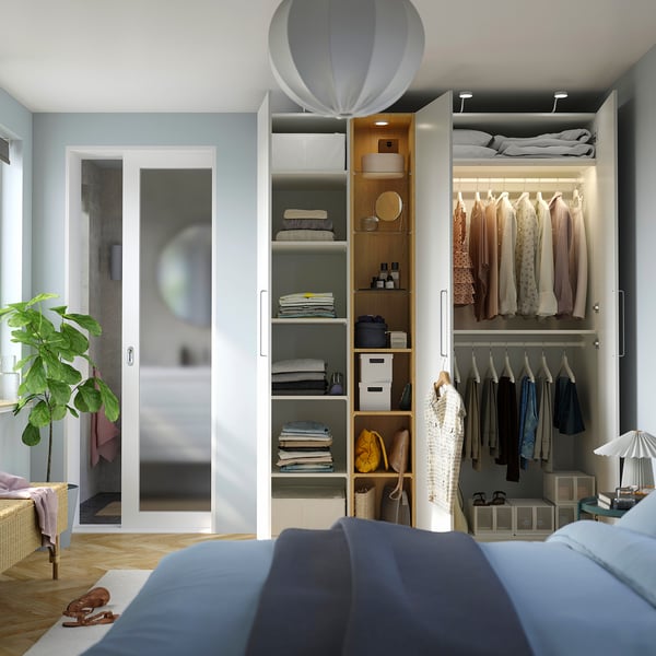 Wardrobe with hanging clothes, shelves, & boxes. Lights on, bed partially seen.