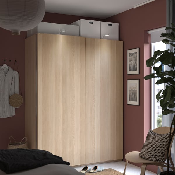 Bedroom with large light brown wooden wardrobe, sliding doors, and modern decor. Plant, artwork, and basket chair nearby.