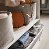 Organized closet shelf with folded clothes in drawer, gray bag, brown purse, and striped shirts.