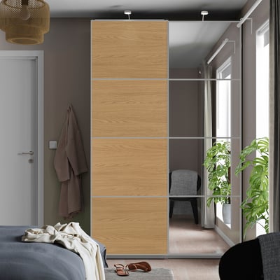 Modern bedroom with large brown PAX wardrobe, reflecting doors, beside a white door and draped window, featuring a cosy bed.